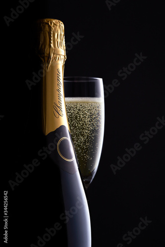 Champagne bottle and full glass with clear bubbles moody black background, high-end concept for luxury clamorous celebration, curves, silhouette, bottle shape close up. 