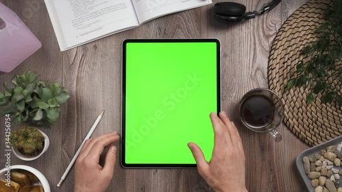 Big tab with chroma key green screen on it lay on the workplace table. Hand swipe left on touchscreen. Big screen of the tablet. Right hand swiping left. Work table with many things on it. Day time