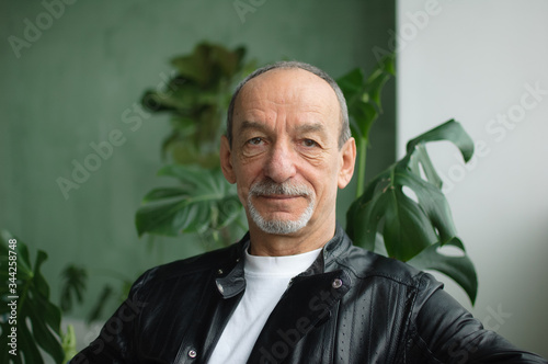 Portrait of senior mature man in leather jacket sitting at the sofa and looking at the camera on green studio background photo