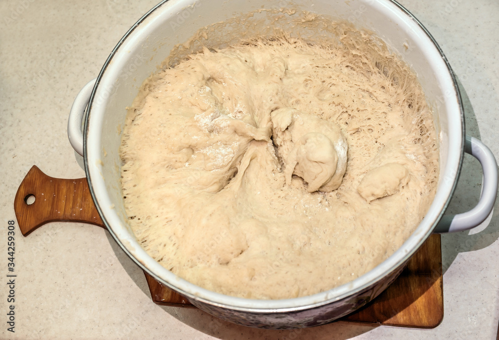 raw dough in an enamel pan,
yeast dough in a white pan on the tabl