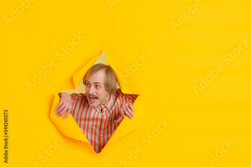 Attented looking. Cheerful caucasian young man poses in torn yellow paper background, emotional and expressive. Breaking on, breakthrought. Concept of human emotions, facial expression, sales, ad. © master1305