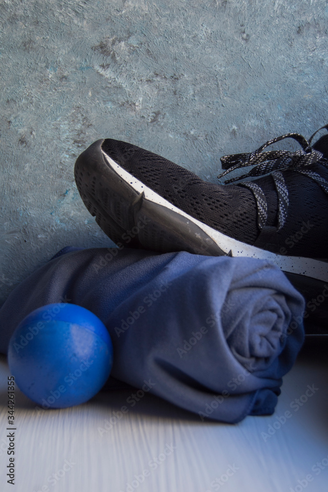 Fototapeta premium Black sneaker with white details and holes, a blue rolled towel and a blue foam rubber ball on a white base and a background in blue and gray tones.