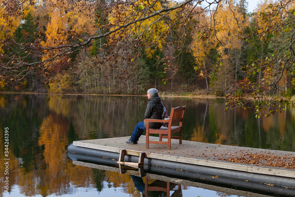 Young women sitting on a pier enjoys golden trees along the lake, lake system near Aegviidu, Estonia. Autumn season, moody weather. Young women sitting on a pier enjoys golden trees along the lake, lake system near Aegviidu, Estonia. Autumn season, moody weather.