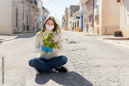 Girl wearing mask, is looking with hope and holding a branch of blooming twigs, standing in the middle of empty street. Concept of end of quarantine and win over coronavirus, thank you nurse photo