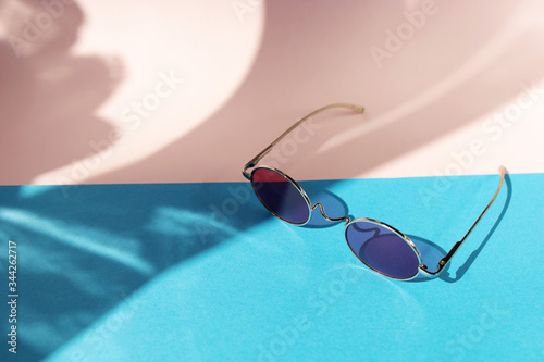 Pink sunglasses on the light pink and blue background. Summer concept. Different shadows. Copy space.Place for text and design.