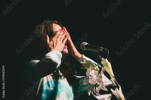 Konstfotografi Brunette Singer woman with red nails hiding her eyes while performing with a mic