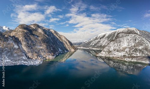 Aerial drone shot of ferry boat on Hallstatt lake with ripples in between snow mountains in Austria in winter before sunset