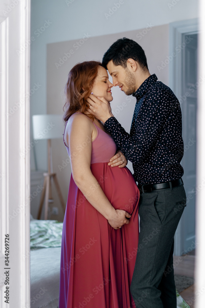 Naklejka premium Happy pregnant couple. Loving husband wants to kiss tenderly his pregnant wife touching her face at home
