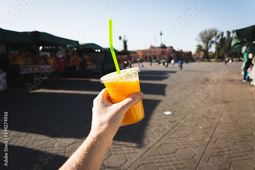 Hand holding a cup of fresh orange juice in Jemaa el-Fnaa square in Marrakesh, Morocco