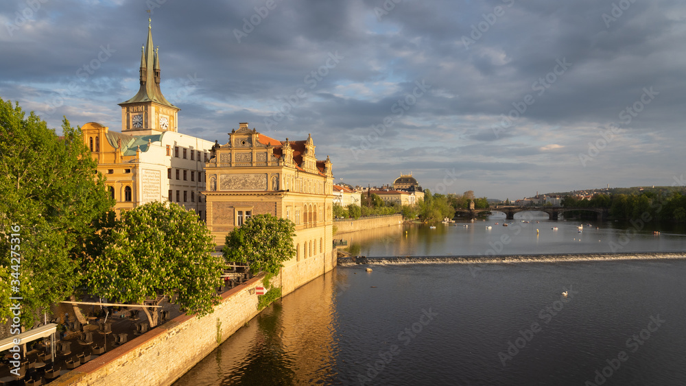 Historic buildings in the old town of Prague seen from Charles bridge. Beautiful golden light during sunset. Unidentified people on boats on Vltava river and roof of the National theater in background