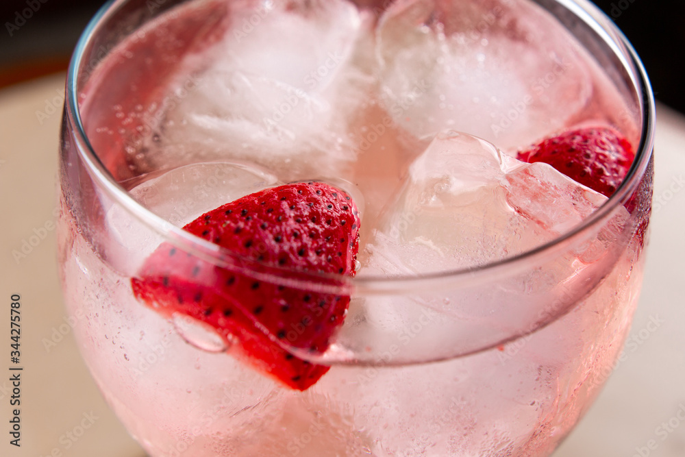 Pink tonic with strawberries in a wide glass cup. Pink gin tonic cocktail with strawberries and ice with a light beige marble background. Close up Pink tonic with strawberries in a wide glass cup. Pink gin tonic cocktail with strawberries and ice with a light beige marble background. Close up