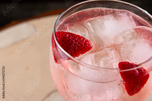 Red strawberries in pink gin and tonic cocktail in glass cup on beige background. Pink gin tonic cockatil with strawberries and ice on light and dark background. Close up. photo