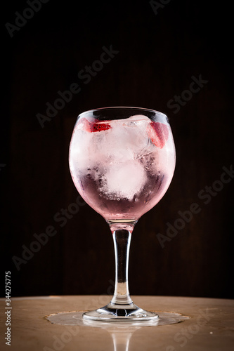 Pink tonic with strawberries in a wide glass cup. Pink gin tonic cocktail with strawberries and ice with a light and dark background. General shot