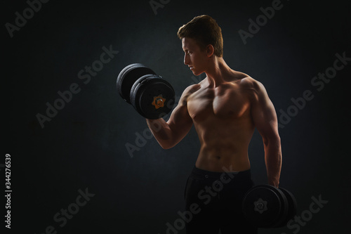  Muscular man with dumbbells on black background