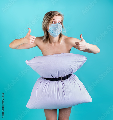 Blond woman in pillowdress wearing a mask showing thumbs up isolated on blue background photo