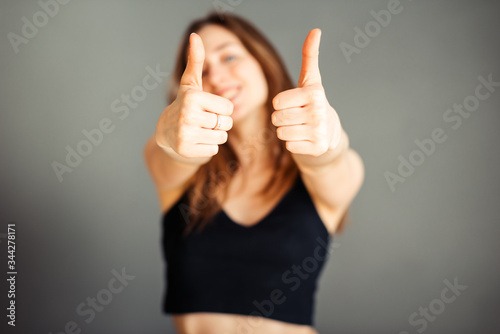 Girl in a black top with her hair shows thumb up. On a gray background. Without makeup, without retouching.