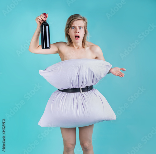 Angry and surprised woman in pillowdress holding a wine bottle isolated on blue background photo