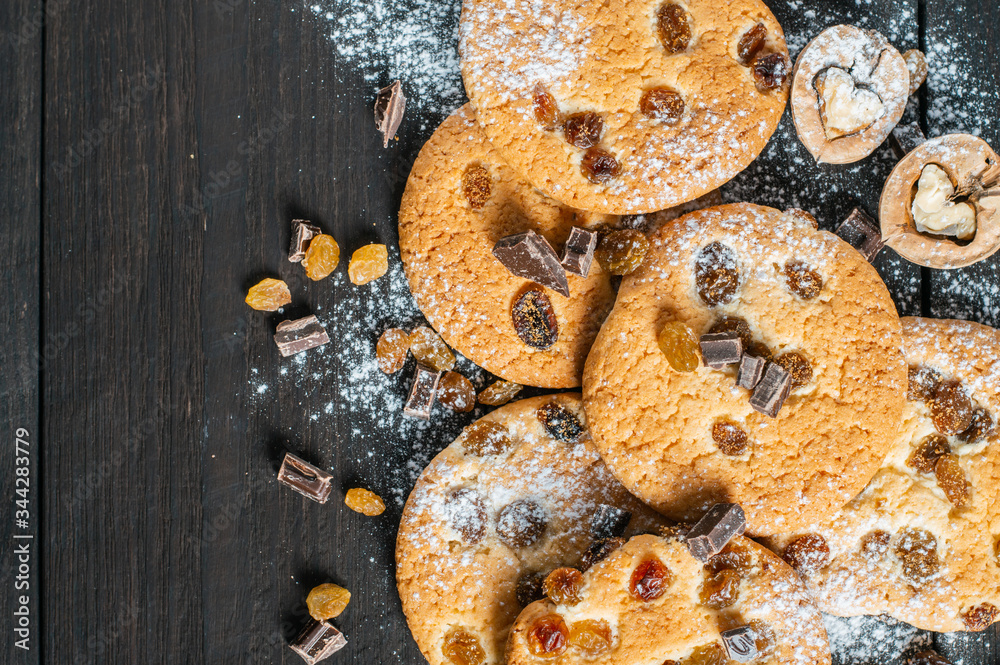 Naklejka premium Oatmeal cookies with raisins, chocolate and nuts sprinkled with powdered sugar lie on a dark wooden background