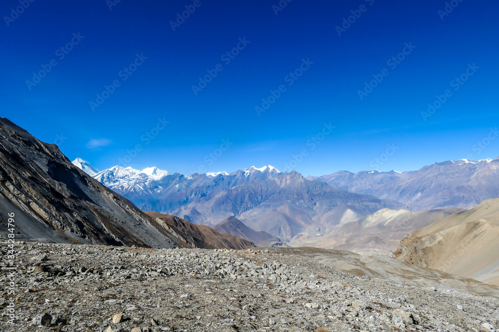 A panoramic view on dry Himalayan valley, located in Mustang region, Annapurna Circuit Trek in Nepal. In the back there is snow capped Dhaulagiri I. Barren and steep slopes. Harsh condition.