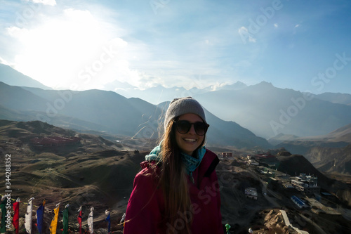 A woman enjoying her time in Himalayas, while trekking along Annapurna Circuit Trek, Nepal. There are multiple mountain chains in the back. The woman is smiling, being happy of her achievement