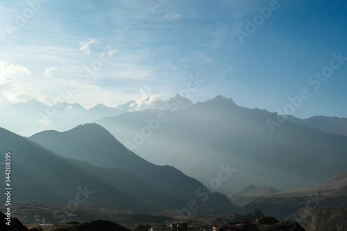 Himalayan chains shrouded in fog, seen from Muktinath, Annapurna Circuit Trek, Nepal. There are multiple mountain chains. Sunbeams breaching through the peaks. Golden hour. Meditation and serenity.
