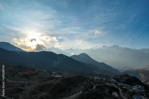 A setting sun in Nepalese Himalayas, Muktinath, Annapurna Circuit Trek. The sun sets behind high mountains. The mountains are covered with dark shadows. Freedom and adventure. Day break.