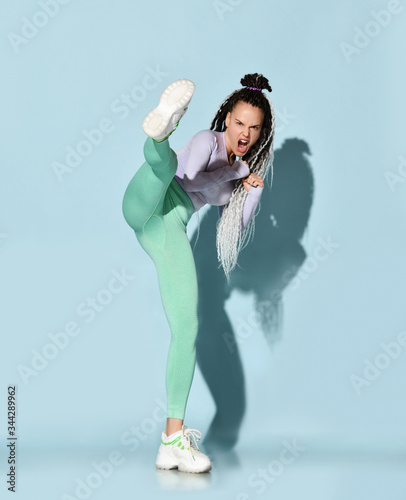 Young beautiful girl with modern hairstyle in sportswear standing and making kick by leg