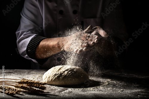 Fototapeta Naklejka Na Ścianę i Meble -  Photo of flour and men hands with flour splash. Cooking bread. Kneading the Dough. Isolated on dark background. Empty space for text