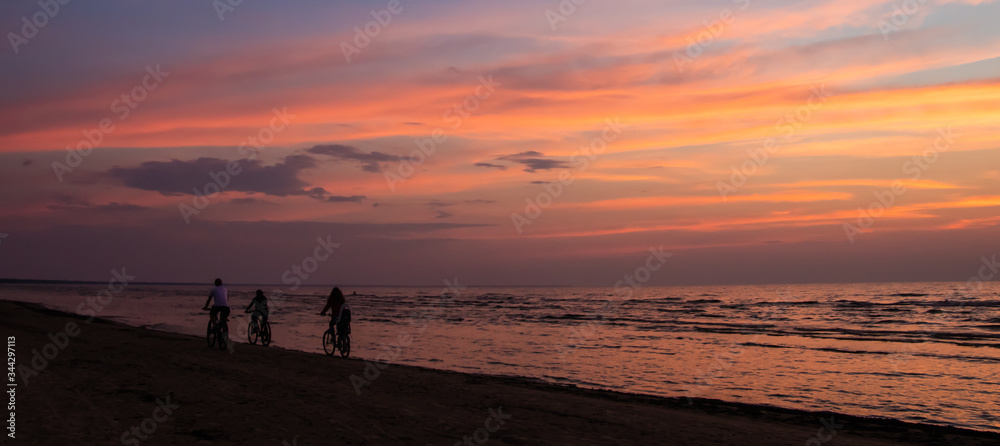 Silhouettes of three cyclists leaving along the coastline of the Baltic Sea at sunset in Jurmala