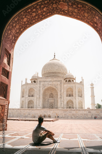 Young man sits under gate and looks at Taj Mahal in Agra