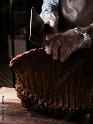 The chief cuts a smoked rib with an ax. Smoked pork ribs. Meat delicatessen on the board. Dry ribs . Grill restaurant kitchen. Closeup of chef hands in black cooking gloves holding smoked pork ribs. photo