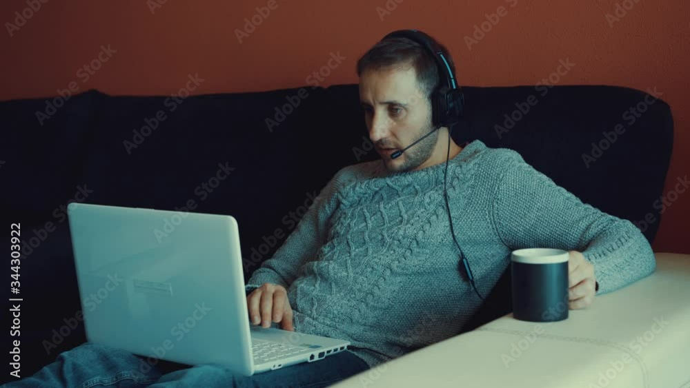 Hermoso joven trabajando en una computadora portátil mientras está sentado en la sala de estar escribiendo durante la cuarentena debido al virus covid-19