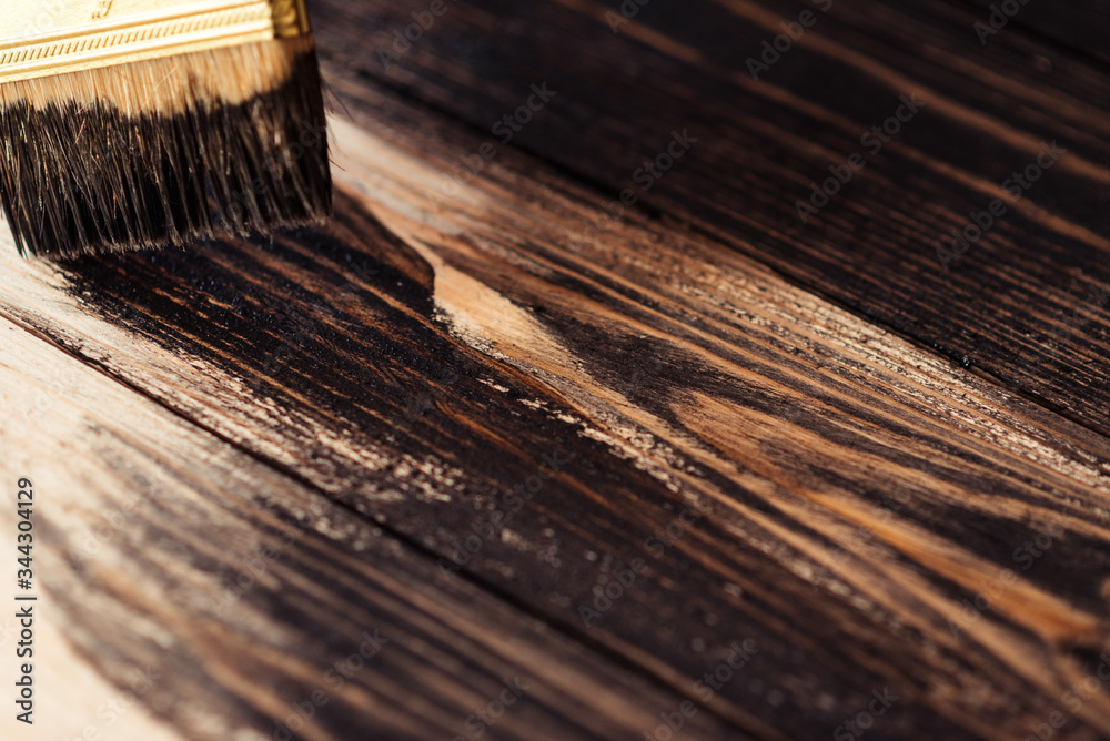 Fototapeta premium Painting a wooden surface stain. Wooden boards are half covered with stain. A brush with a wooden handle, natural bristles on a background of painted wooden planks. The painting process, the layout.