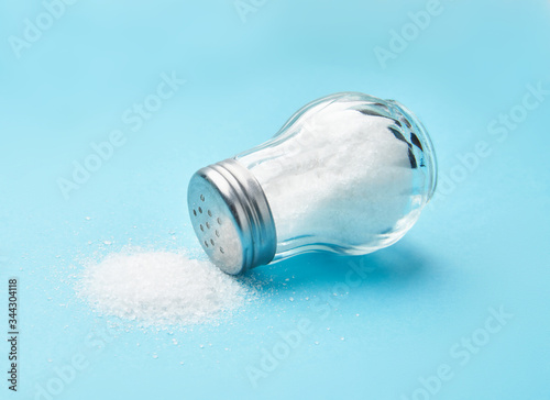 Salt shaker and fine salt isolated on blue background.