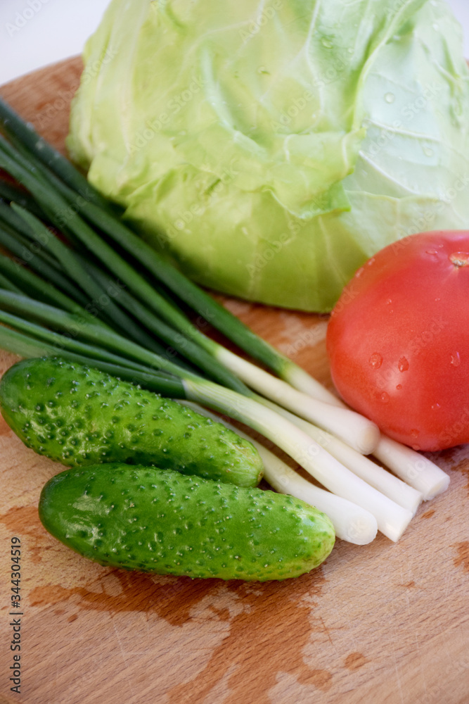 Cabbage, cucumbers, tomato, green onions, salad on a wooden cutting board on a white background Cabbage, cucumbers, tomato, green onions, salad on a wooden cutting board on a white background