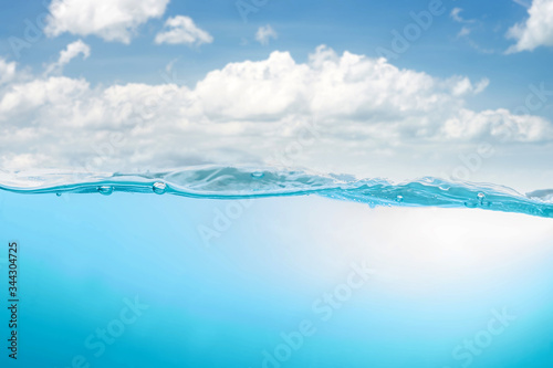 Fototapeta Naklejka Na Ścianę i Meble -  Blue water wave with splash and bubbles surface on blue sky with white clouds