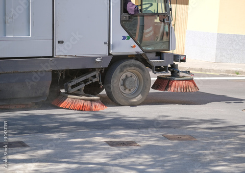 Sweeper truck industrial vehicle cleans urban streets of European city. Street cleaning machine at work. Disinfecting against to the Coronavirus pandemic (COVID-19). Protection.
