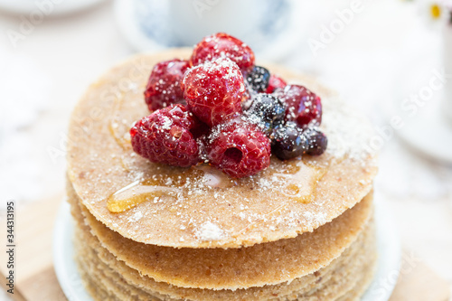 Raw vegan pancakes with honey and birch sugar on a wooden plate with raspberries on top. Healthy eating lifestyle.
