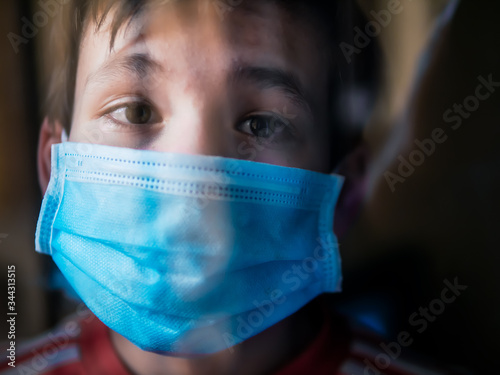 Canvas-taulu Boy with a medical mask looks sadly out of the window during his confinement bec