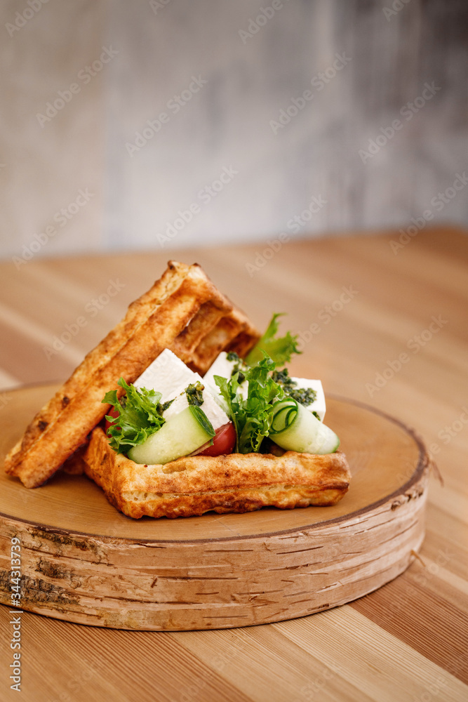 Presentable plating of Belgian waffle topped with vegetables and fresh cheese for healthy living lifestyle. Food photography concept for magazine or online delivery menu.