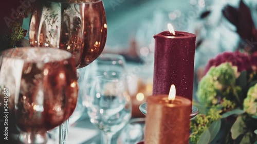Brighr burning candles and goblets on the decorated celebration table, front view of floral wedding decoration