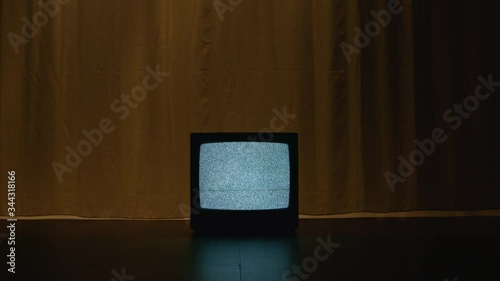 Old CRT TV is on the floor in a dark and empty room. On the screen there is a frightening white noise filling the room with a hypnotizing atmosphere of mystical evil. Dolly camera movement