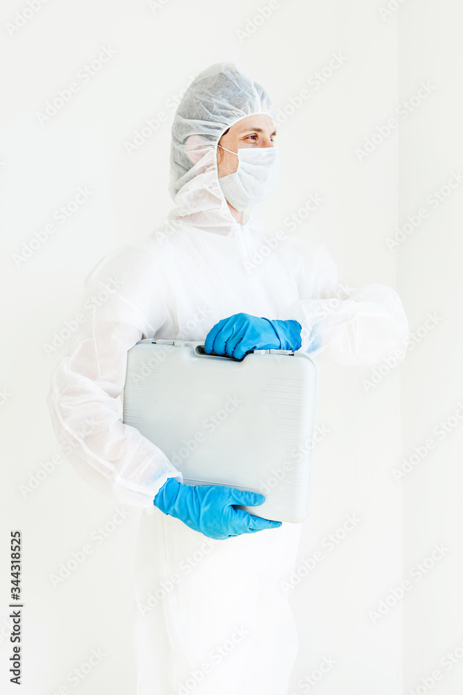 Naklejka premium a man in a protective suit, gloves and face mask is Walking with a suitcase for tests in his hands. The concept of combating coronavirus. Isolated on a white background