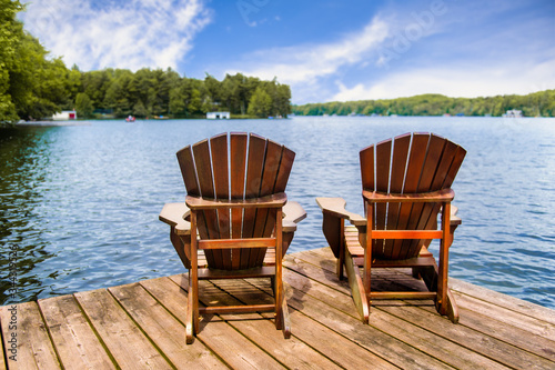 Canvas Print Two Adirondack chairs on a wooden dock overlooking a calm lake