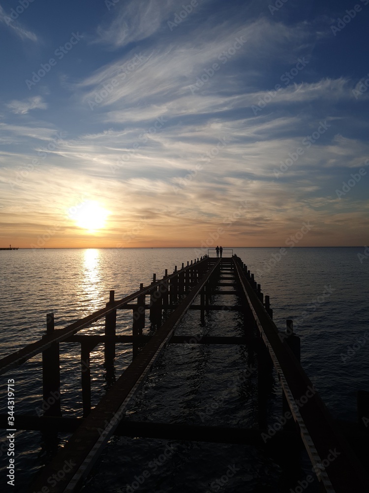 Fototapeta premium Romantic sunset on the pier. The pier goes out into the dark sea. It's good to dream in the evening.