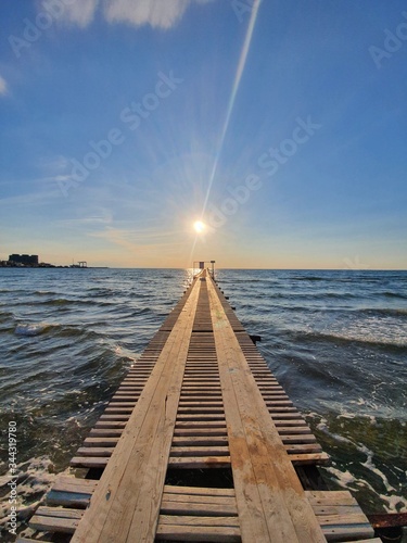 Pier under the rays of the setting sun. A romantic shot of an empty beach during quarantine. The black sea is resting.