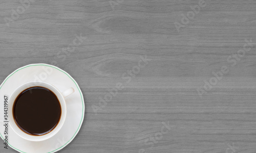 White cup filled with hot coffee, gray wooden board for background and free space for text, top view