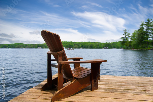 A single Muskoka chair on a wooden dock overlooking a calm lake in Ontario  Canada.