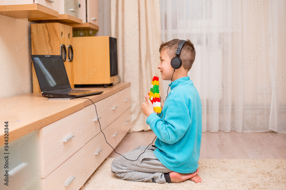 The boy sits, lies on the floor at home with a laptop and tablet. Online learning. Quarantine and isolation. Reyonok plays with another online designer. Home schooling. Baby in headphones smiling

