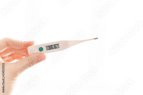 The fingers of a female hand are holding an electronic thermometer with a temperature of 36.6 degrees on the scoreboard on a white background. Health, willingness to work, the end of the coronavirus.